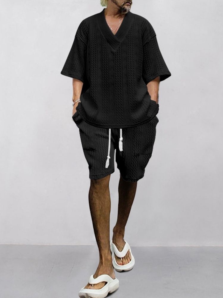 Bleached Buzz Cut + Silver Wrist Stack + Oversize Black Cable-Knit V-Neck + Drawstring Cable-Knit Shorts + White Slide Sandals