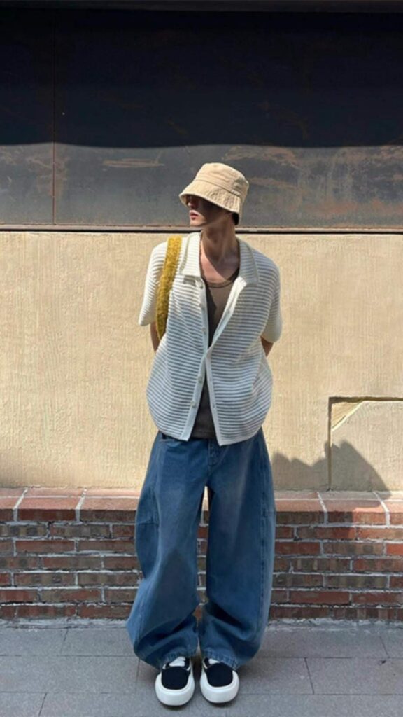Sandy twill bucket hat + Mustard-rope textured shoulder bag + Ivory striped open shirt + Olive tank + Wide-leg faded blue jeans + Black-and-white slip-on skaters