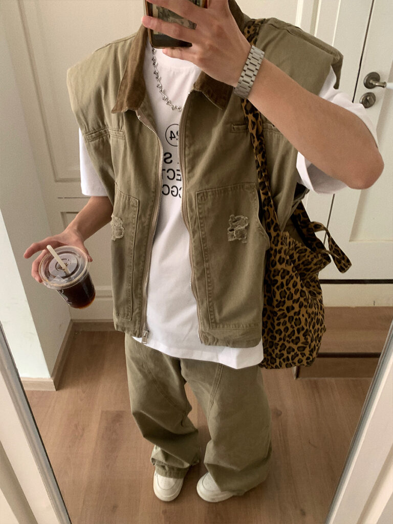 Silver cuban chain + Stone-washed cord-collar utility vest + Oversize white graphic tee + Leopard canvas shoulder bag + Olive carpenter jeans (pooling cuffs) + Off-white canvas slip-ons