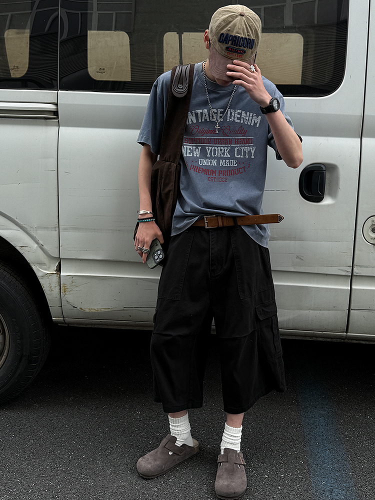 Beige baseball cap (embroidered) + Oxidized dog-tag chain + Vintage print slate tee + Brown web belt + Black cargo culotte shorts + Marled wool socks + Suede clogs