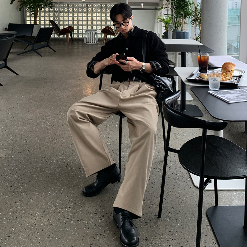 Middle-part hair + black acetate frames + black knit polo + beige pleated chinos + black leather derbies