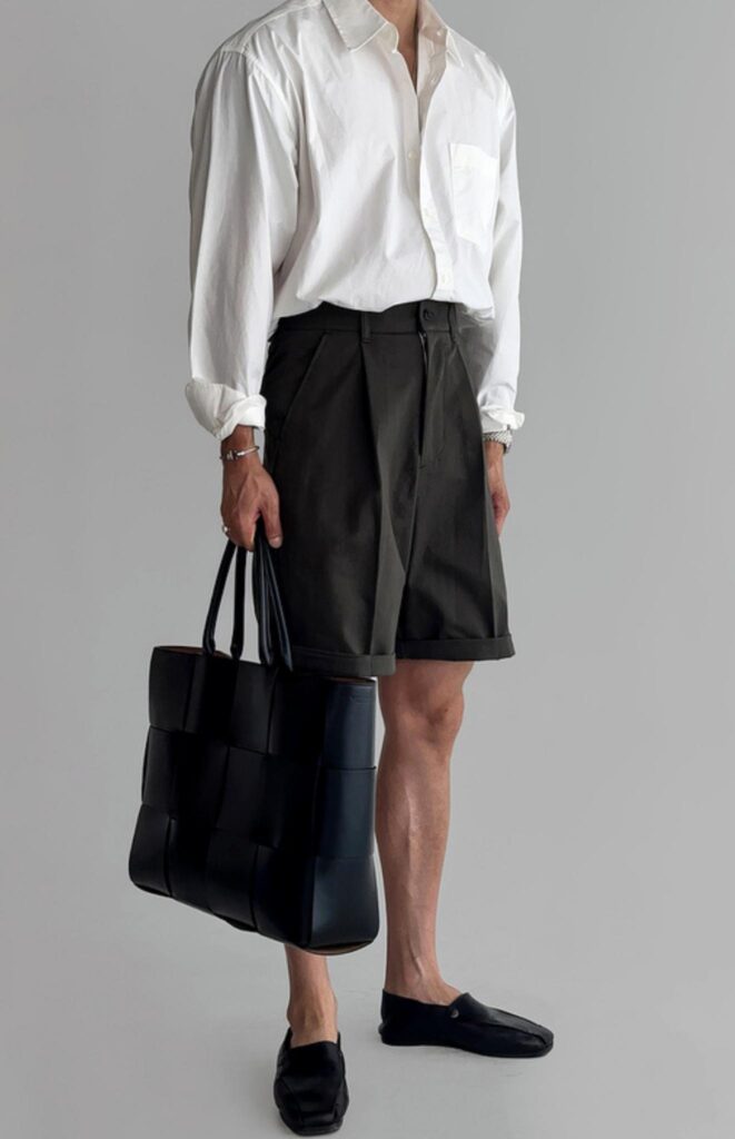 Frosted-lens sunglasses + Crisp white oxford (rolled cuffs, unbuttoned collar) + Tapered charcoal pleated shorts + Black basket-weave leather tote + Black slipper loafers