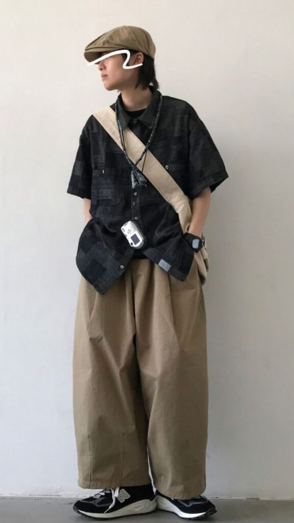 Sand flat cap + Charcoal patchwork short-sleeve shirt + Beige canvas cross-strap + Oversized khaki balloon pants + Black technical sneakers
