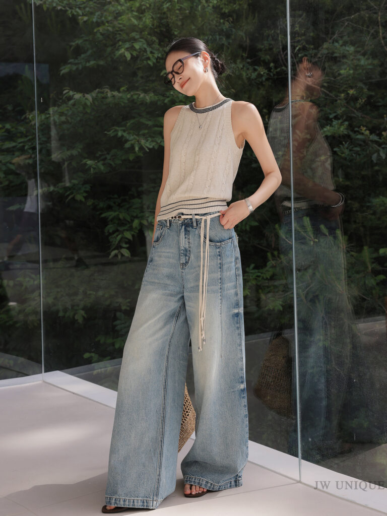 Slick low bun + square tortoiseshell glasses + varsity-trim cable-knit tank + rope drawstring belt + light-wash wide-leg jeans + black thong sandals