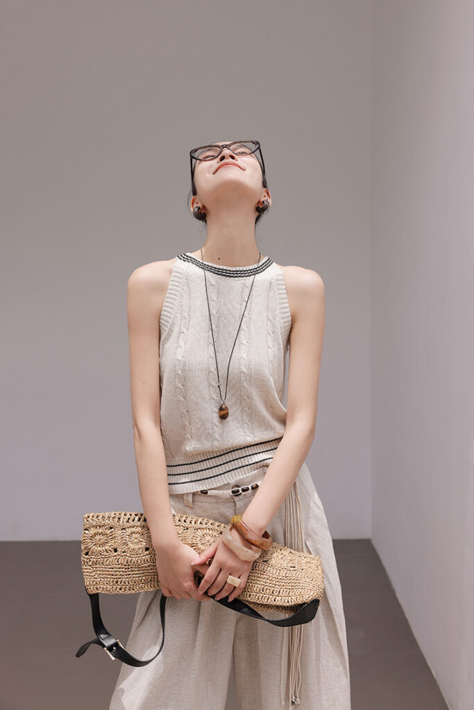 Cat-eye glasses + ivory varsity-trim cable-knit tank + beige linen trousers