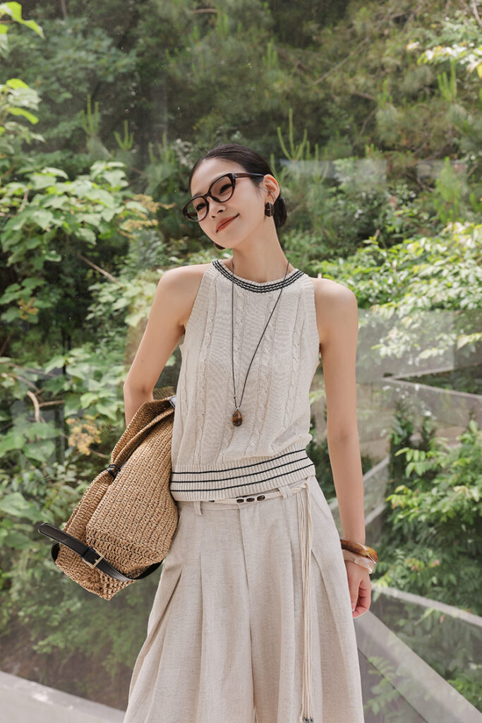 Cat-eye glasses + ivory varsity-trim cable-knit tank + beige linen pleated trousers + rope belt