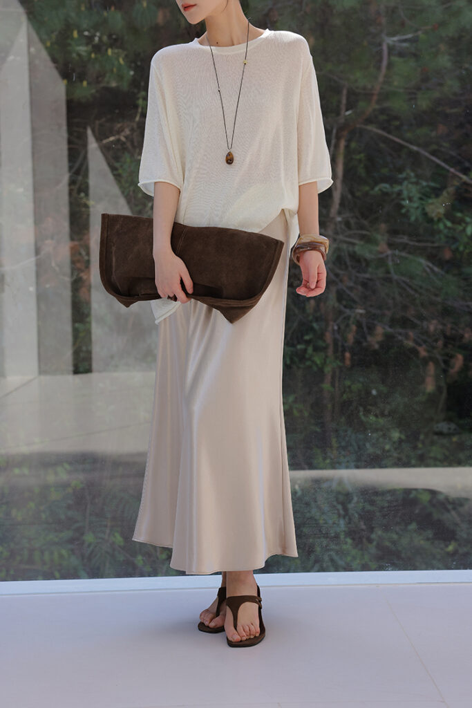Side-part bob + long amber pendant + oversized ivory knit tee + champagne satin slip skirt + suede megaclutch + brown sandals